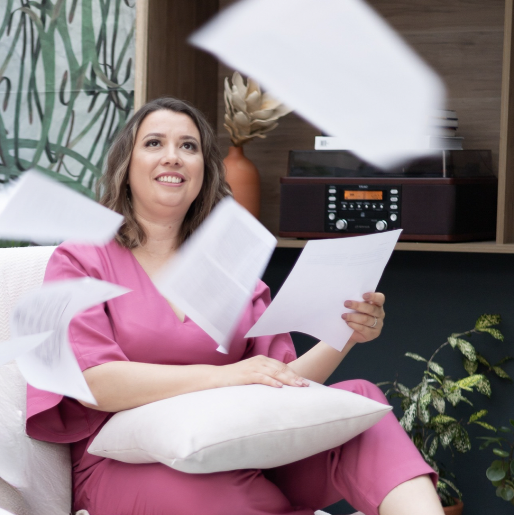 La fonoaudióloga esta sentada y ha tirado articulos científicos hacia arriba.