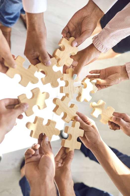 mano de miembros de un equipo. Cada miembro tiene en sus manos una pieza para completar un puzzle.